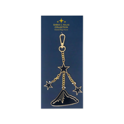 A gold-tone and black enamel keychain charm from the Sarah & Maas Collection, featuring three stars and a mountain peak, displayed on its dark blue packaging card.