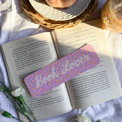 Open book with a floral bookmark titled 'Book Lover' on a white surface with a donut and flowers.