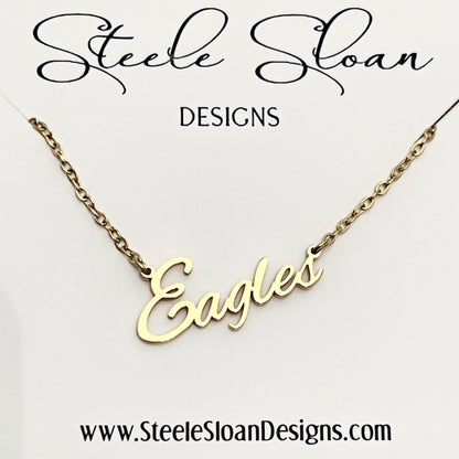 A gold nameplate necklace spelling 'Eagles' on a delicate gold chain, presented on a white display card with the brand name 'Steele Sloan DESIGNS' at the top and the website 'www.SteeleSloanDesigns.