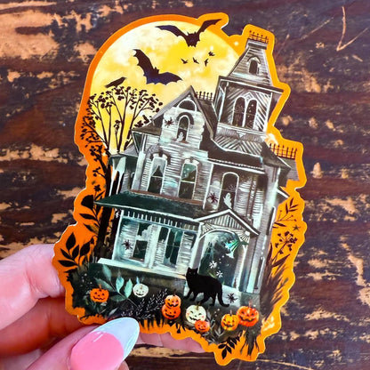 Halloween-themed sticker of a haunted house with pumpkins and bats on a wooden surface.