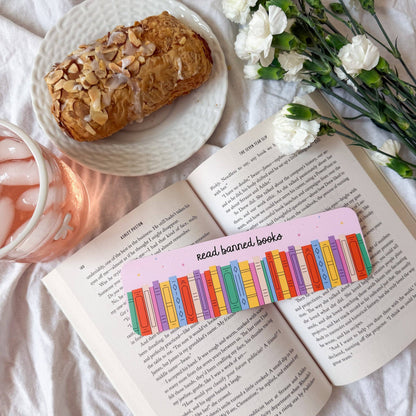 Open book with a colorful bookmark, pastry, and flowers on a light surface