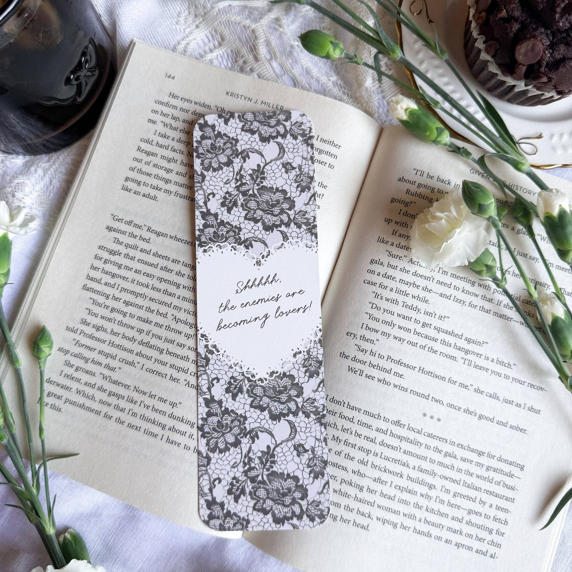 Open book with a decorative bookmark on a white surface with flowers and a cup.