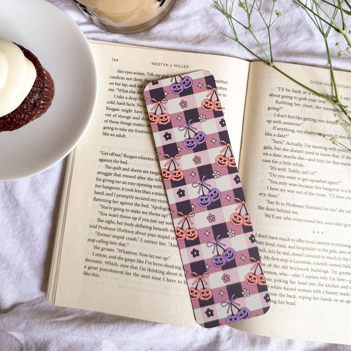 Book with a decorative bookmark, iced coffee, and dessert on a white surface.