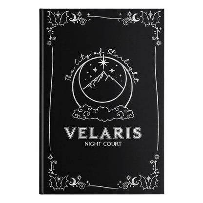 A black hardcover notebook or journal featuring a white celestial design with a moon, stars, mountain, and clouds, with the text 'VELARIS NIGHT COURT' printed on the front.